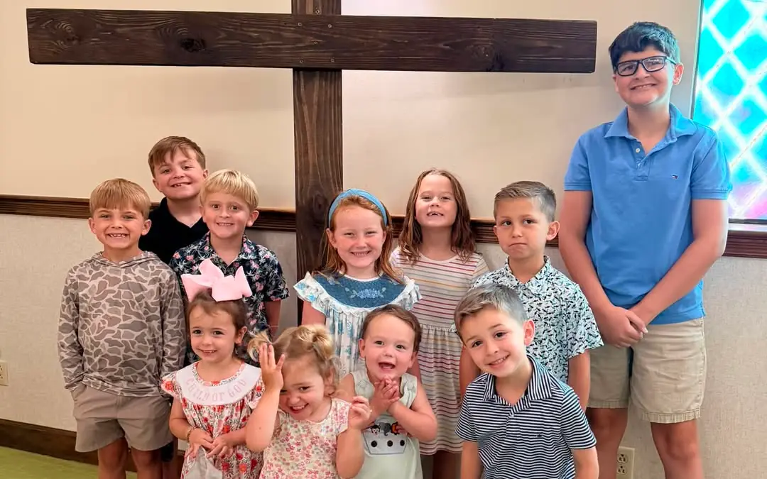 A group of smiling kids standing in front of the wooden cross in the sanctuary